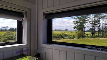 A room with two windows overlooking a rural landscape with fields and trees.