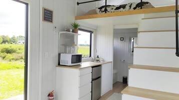 Una cocina compacta con microondas, lavamanos y una pequeña ventana con vistas a un paisaje verde.