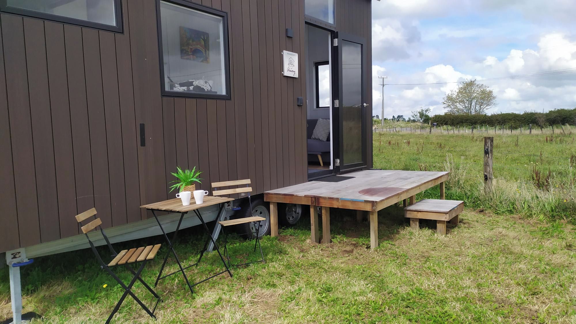 A modern building with a wooden exterior, a small outdoor seating area with a table and chairs, and a potted plant.