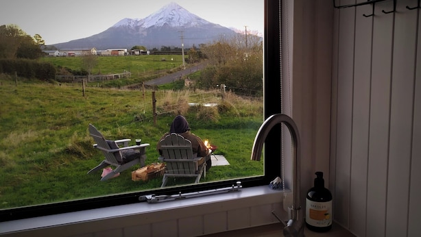 A kitchen with a window view of a grassy field and a mountain. - Taranaki Creekside TUI by Tiny Away (Midhirst)