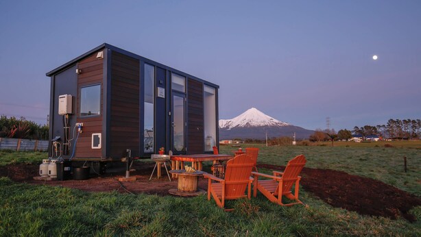Eine moderne Hütte mit Essbereich, Sitzgelegenheit im Freien und Blick auf einen schneebedeckten Berg.