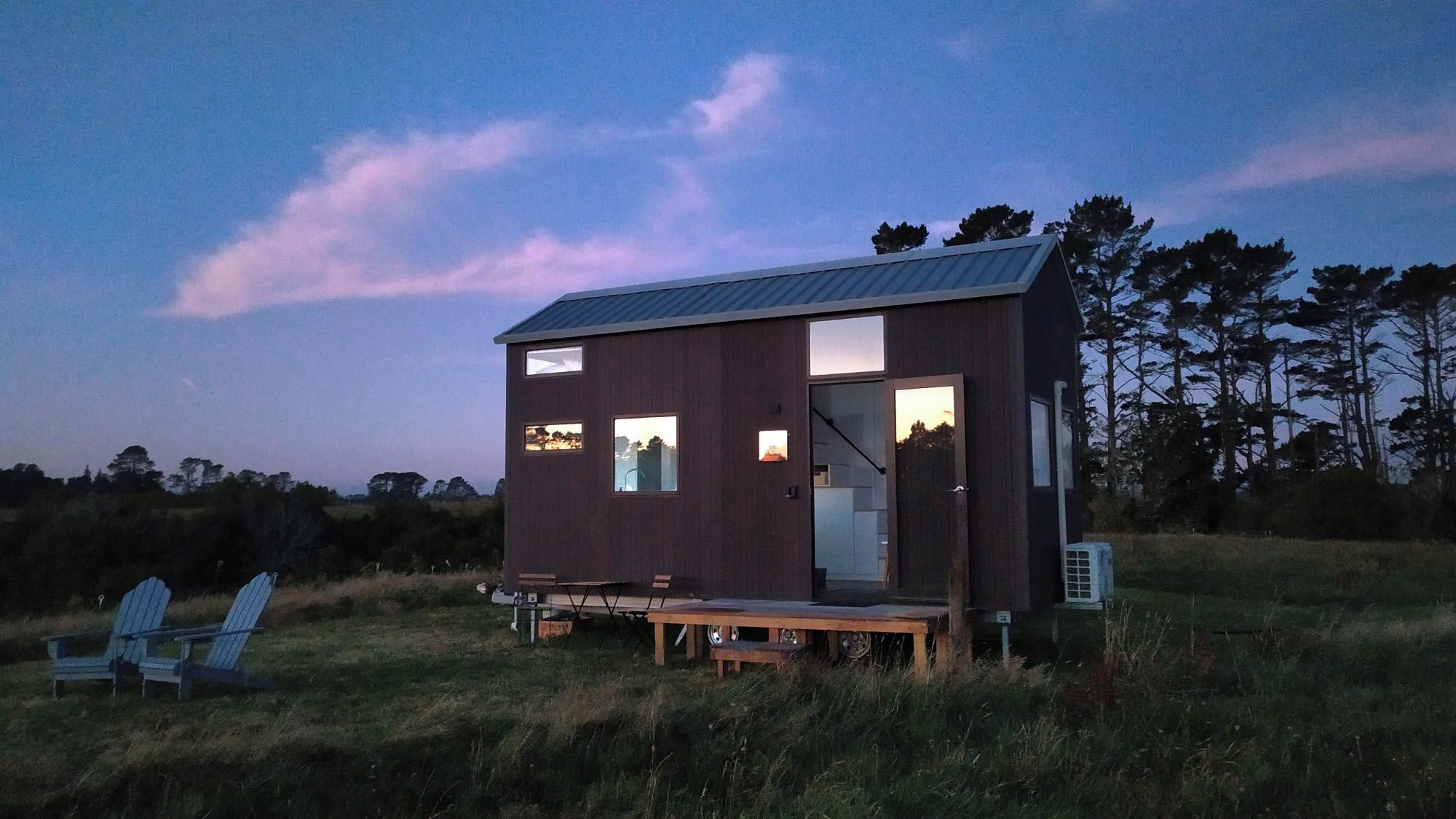 A small, modern cabin with a metal roof, large windows, and a deck area.
