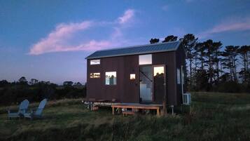 A small, modern cabin with a metal roof, large windows, and a deck area.