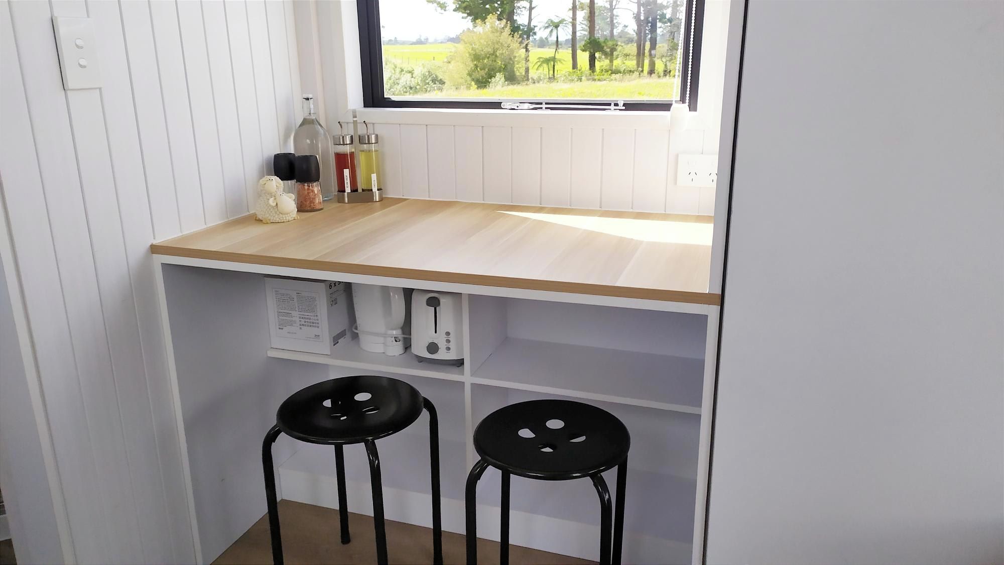 A compact kitchen with a wooden countertop, two black stools, and a window with a view of greenery.