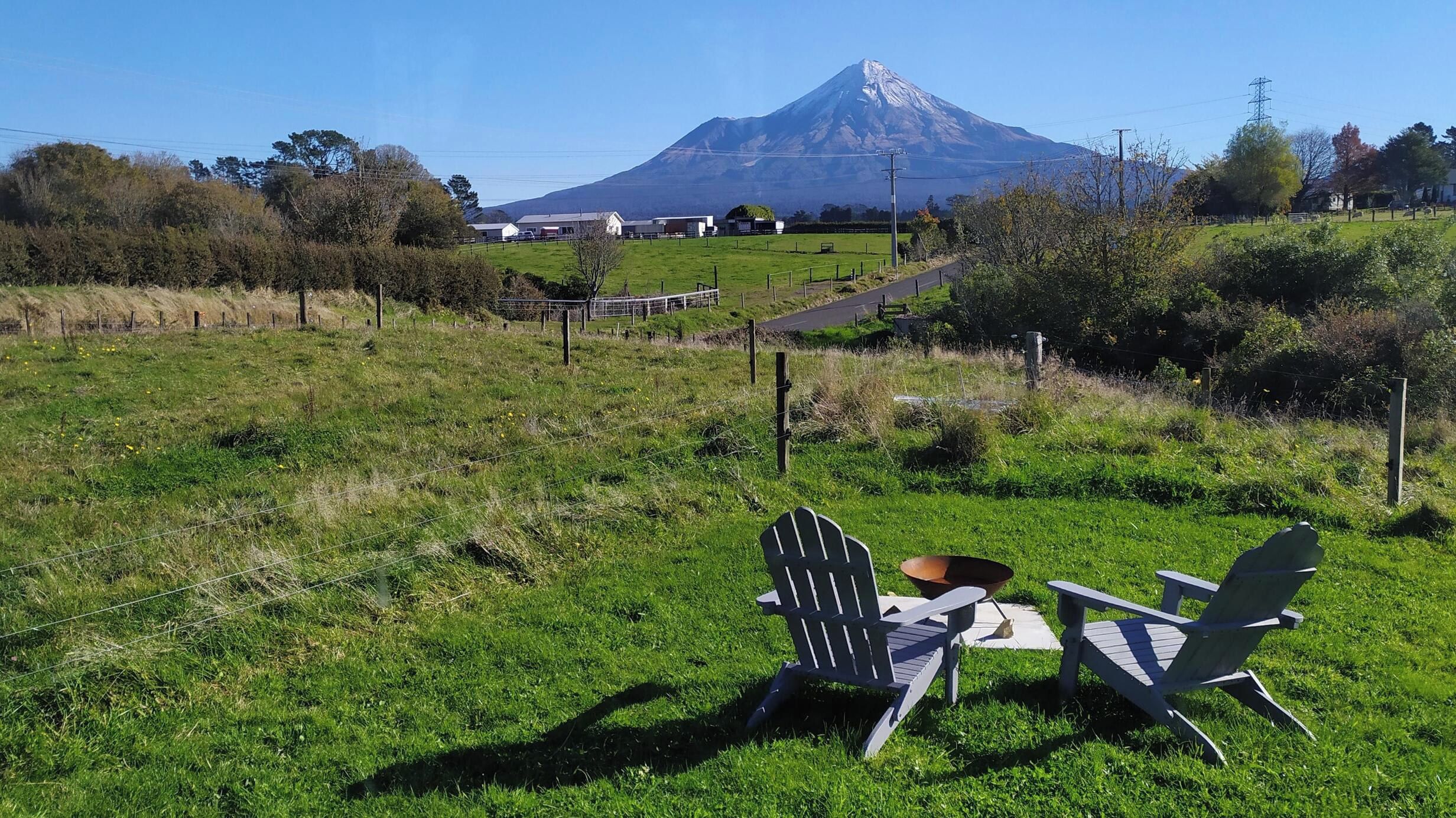 A grassy field with two Adirondack chairs and a metal bowl, with a mountain in the background.