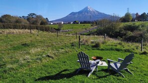 Ein grasbewachsenes Feld mit zwei Adirondack-Stühlen und einer Metallschüssel, im Hintergrund ein Berg.