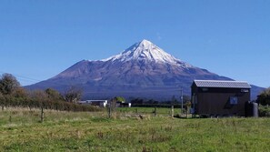 A mountain with a snow-capped peak, a small wooden building, and a clear blue sky. - Taranaki Creekside TUI by Tiny Away (Midhirst)