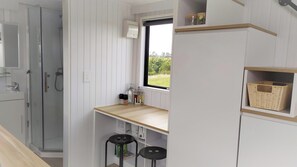 A compact kitchen with a window, a sink, and a small countertop with stools. - Taranaki Creekside TUI by Tiny Away (Midhirst)