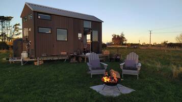 A small cabin with a fire pit and two Adirondack chairs in the yard.