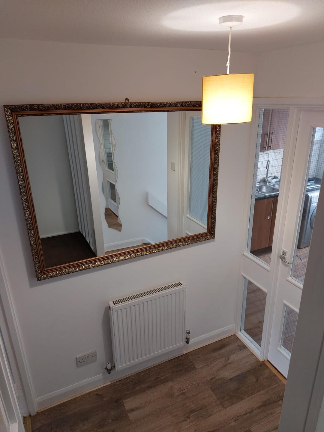 A room with a large ornate mirror, a white radiator, and a wooden floor.