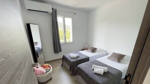 Een slaapkamer met twee bedden, een raam, een spiegel en een zithoekje met kussens.