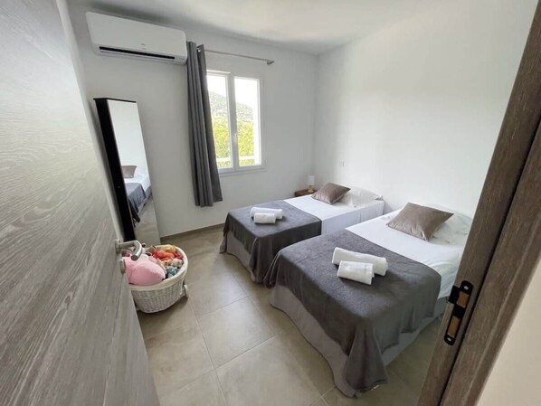 Een slaapkamer met twee bedden, een raam, een spiegel en een zithoekje met kussens.