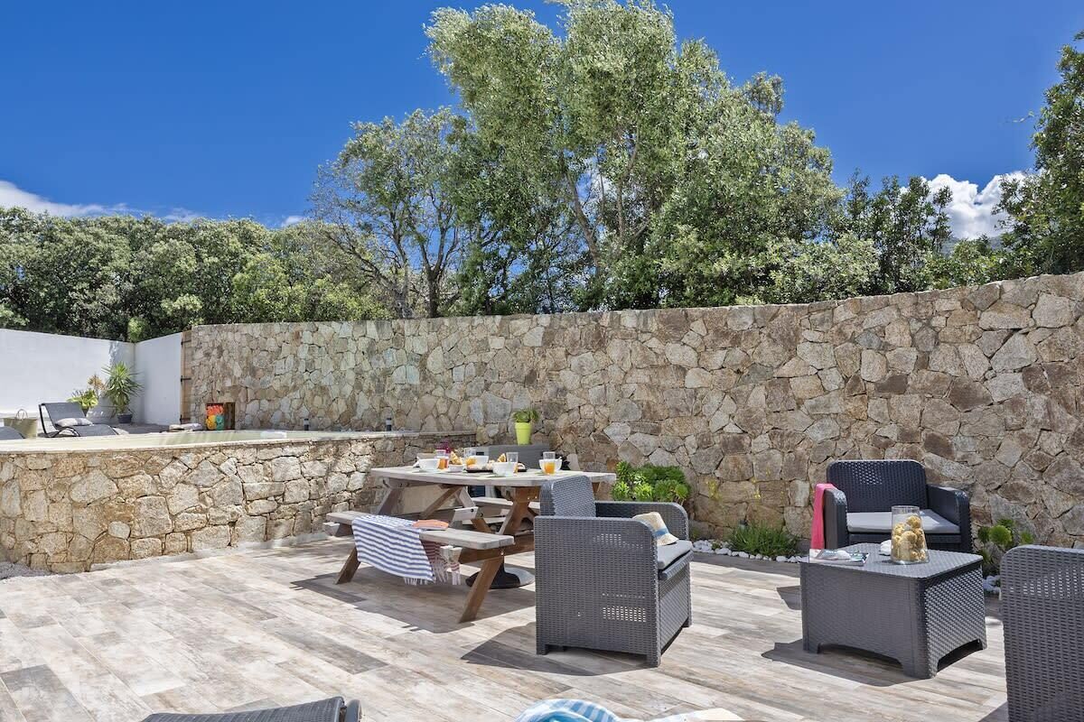 An outdoor patio area with stone walls, wicker furniture, and a table set for dining.