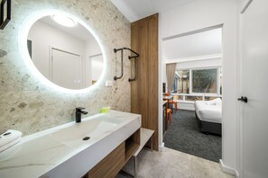 A modern bathroom with a white sink, a large mirror with a circular light, and a wooden panel.
