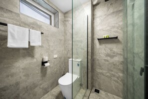 A modern bathroom with a glass-enclosed shower, a toilet, and a towel rack with two towels. - Kingsway Motel Geelong (Newtown)