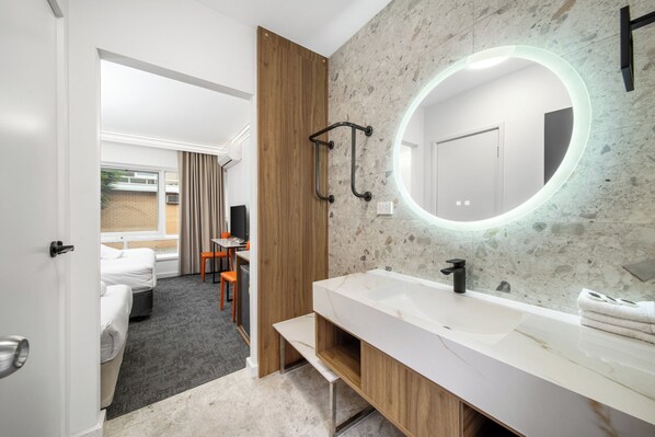 A modern bathroom with a large mirror, a white sink, and a wooden vanity.