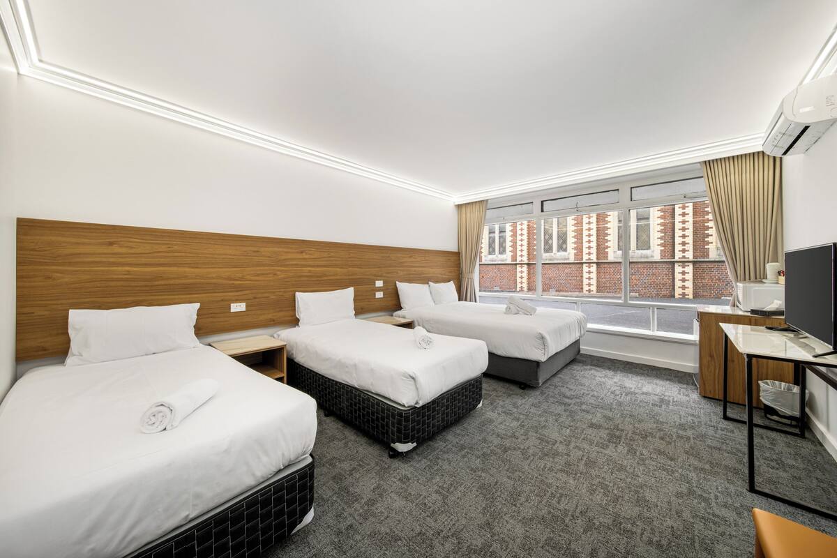 A hotel room with three beds, a desk, and a TV.