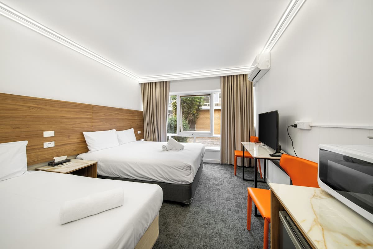 A hotel room with two beds, a desk, a TV, and a window with curtains.