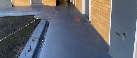 Een gang met aan de ene kant een bakstenen muur en aan de andere kant een grijze muur, die leidt naar een deur aan het einde.