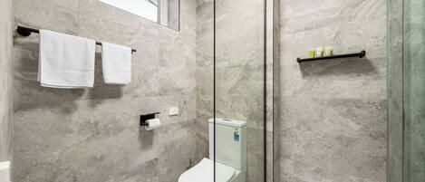 Un baño moderno con cabina de ducha de vidrio, inodoro y repisa con artículos de aseo.