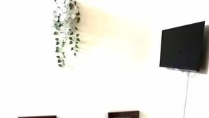 Une petite pièce avec un plancher en bois, une table entourée de chaises, un téléviseur fixé au mur et une plante verte accrochée au mur.