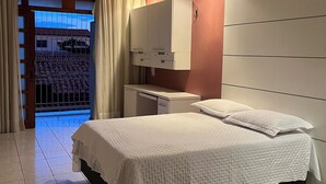 A hotel room with a bed, a desk, a wardrobe, and a view of a building through a window. - Casa Ampla com 4 Suítes com Escritório, Aceita Animais de Estimação (São Pedro Teresina)