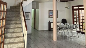 A spacious indoor area with a wooden ceiling, a staircase, and a dining area with chairs and tables. - Casa Ampla com 4 Suítes com Escritório, Aceita Animais de Estimação (São Pedro Teresina)