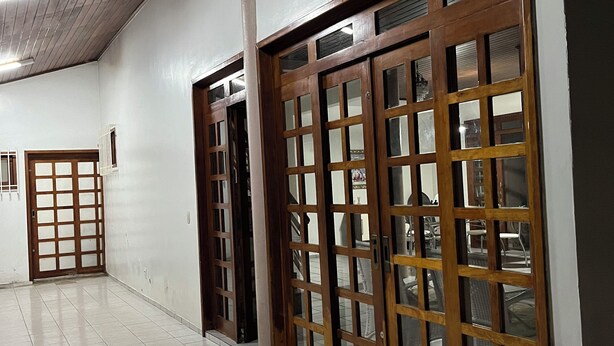 A hallway with tiled flooring, wooden doors with glass panels, and a ceiling with exposed beams and lighting fixtures. - Casa Ampla com 4 Suítes com Escritório, Aceita Animais de Estimação (São Pedro Teresina)
