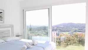 A bedroom with a large bed, a view of a landscape through a sliding glass door, and a white wall with a framed picture. - House with garden and private pool 6km beach (Calonge)