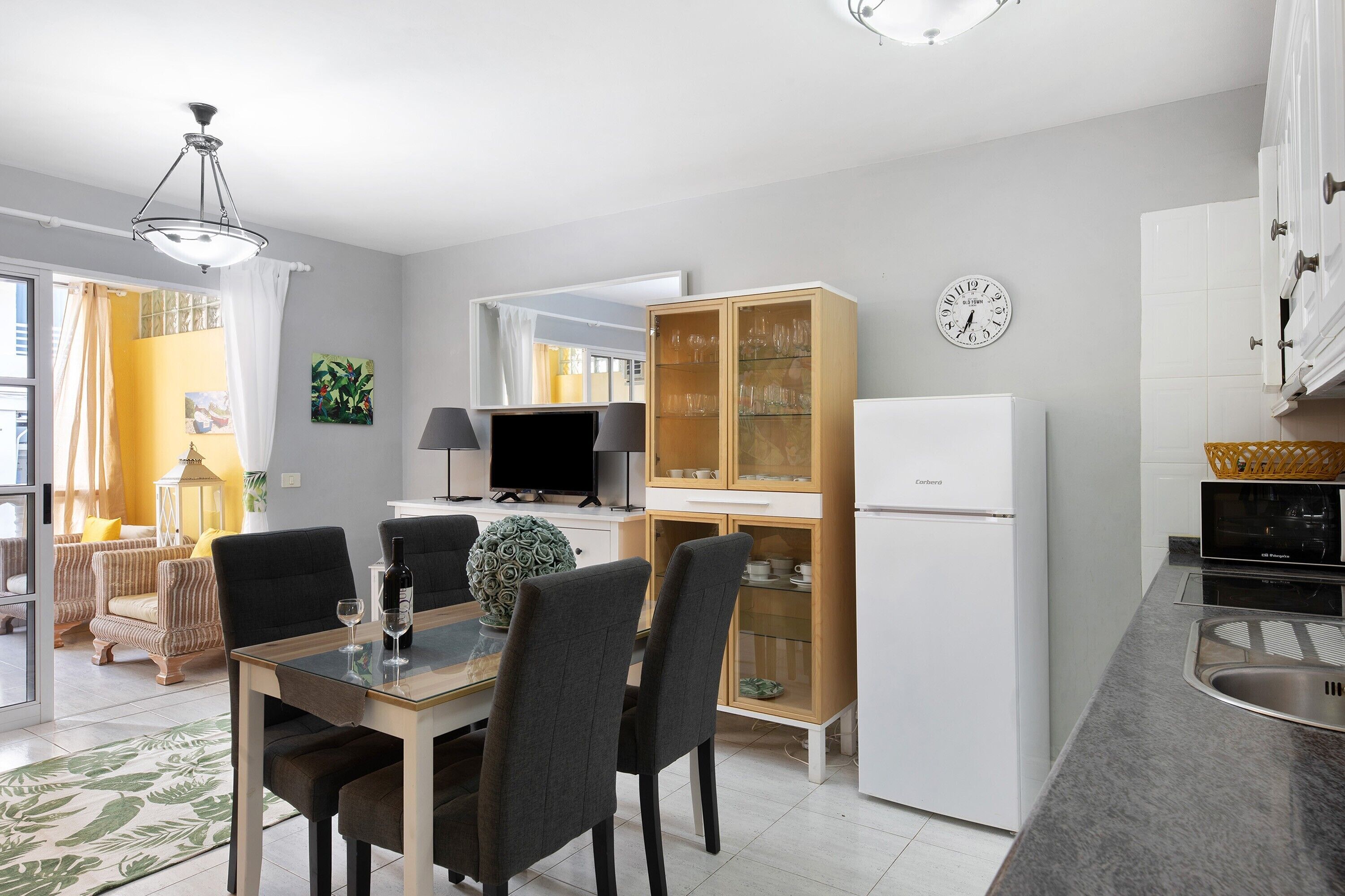A modern kitchen with a dining area, a television, and a refrigerator.
