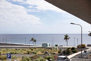Eine Küstenstraße mit Parkschild, Strand und Meerblick unter einer Brücke.