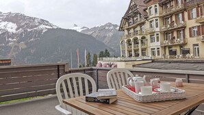 A wooden table with chairs and a tray of cups and saucers on a balcony overlooking snow-capped mountains. - BeKb-Gebäude Apt. 01 by Interhome (Wengen)