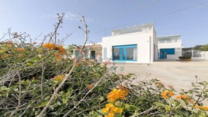 Un bâtiment blanc avec une porte et des fenêtres bleues, entouré de verdure et de fleurs.