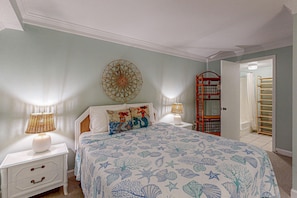 A bedroom with a bed, two bedside tables with lamps, a wall hanging, and a door leading to a bathroom.