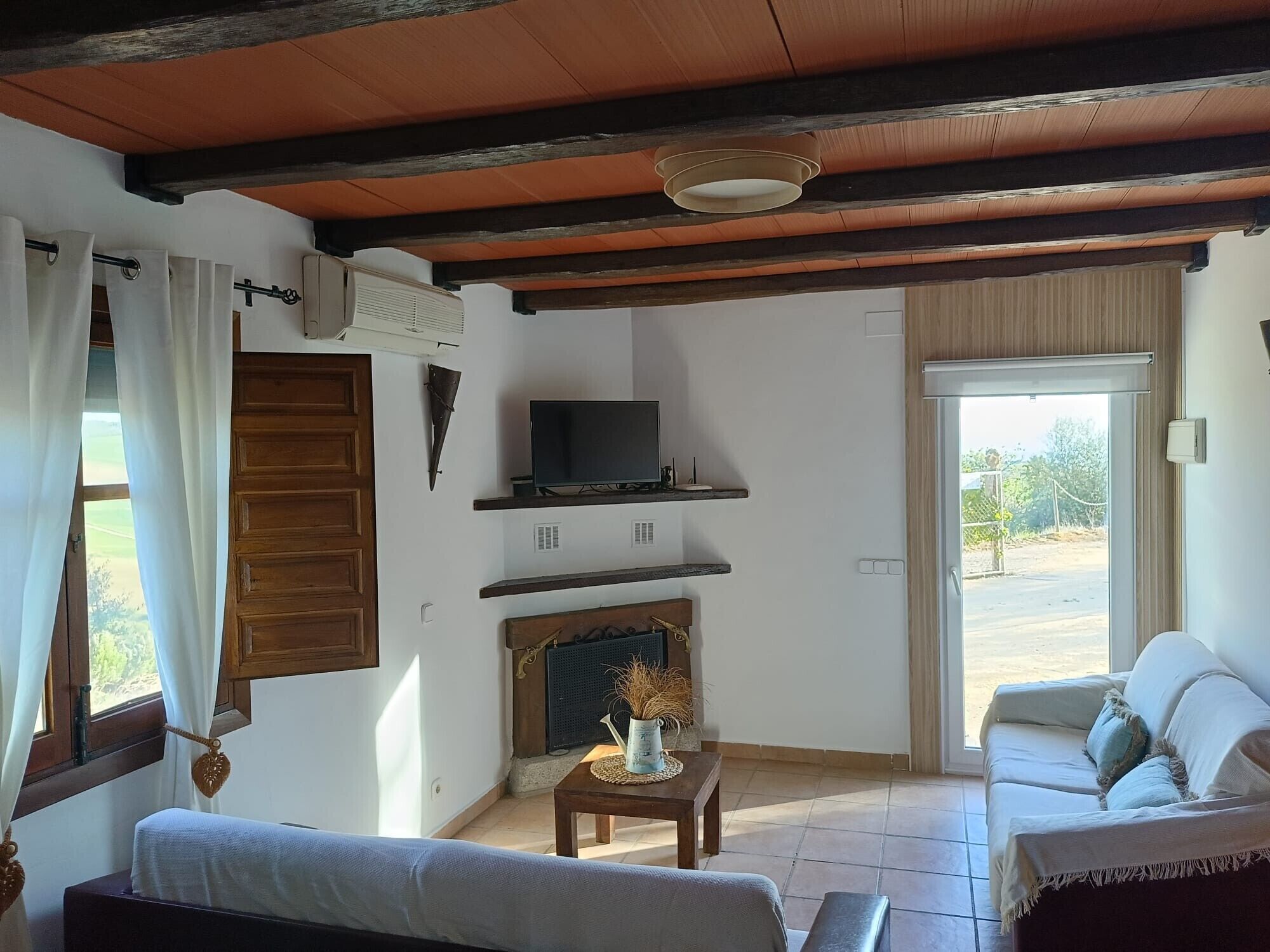 A living room with a sofa, a television on a shelf, a fireplace, and a door leading outside.