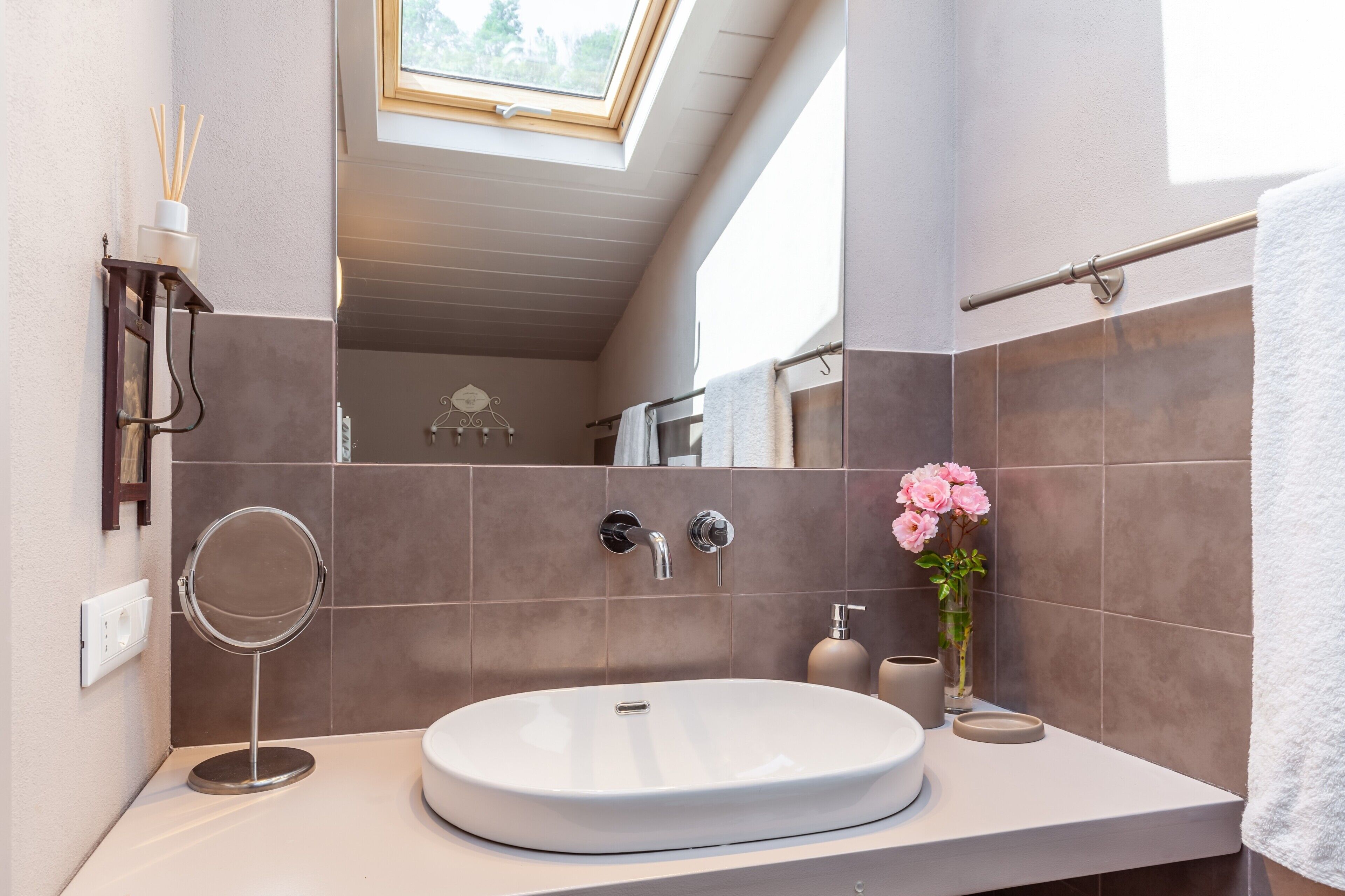A bathroom with a skylight, a round mirror, a sink, and a towel rack.