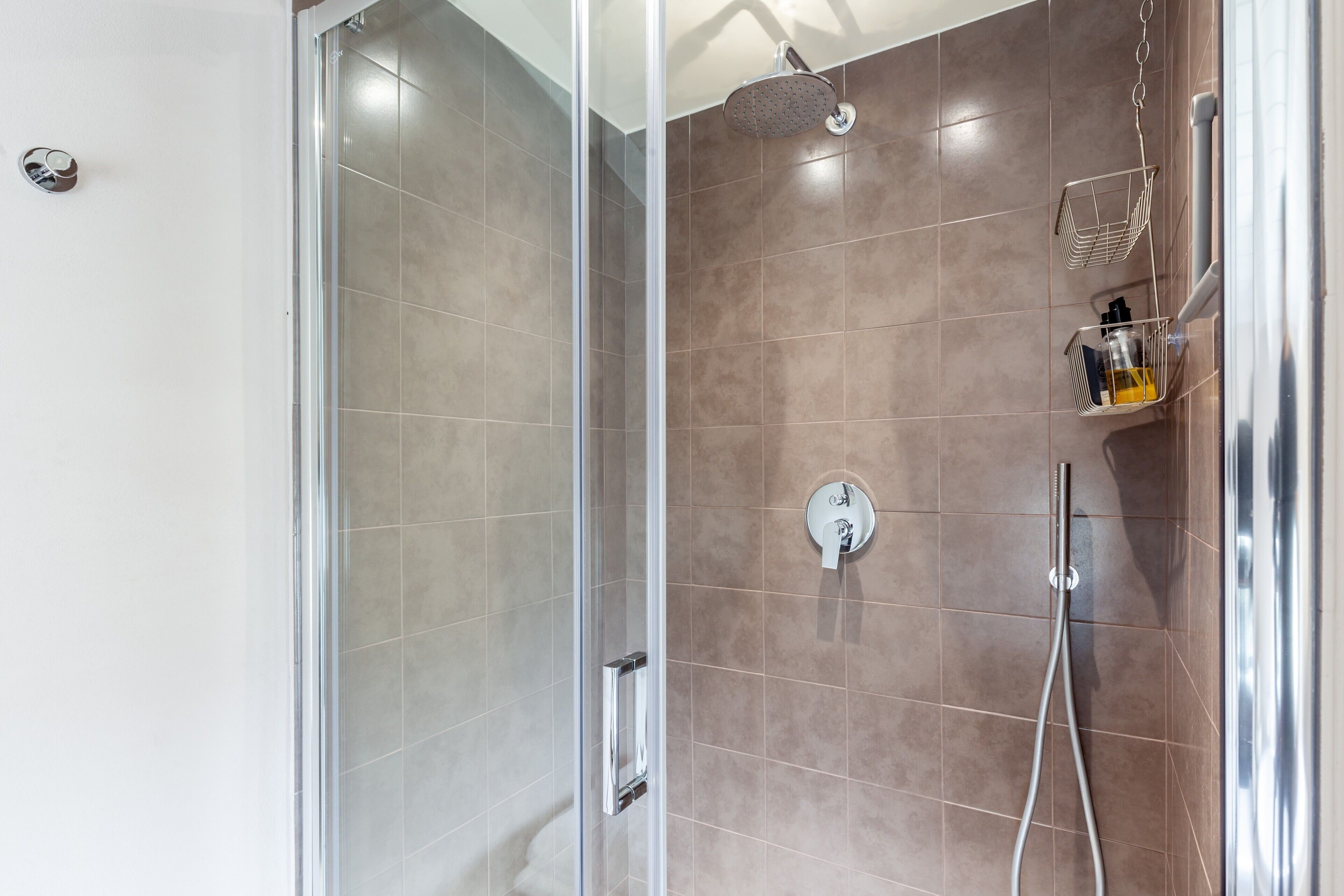 A modern shower with a glass door, a handheld showerhead, and a wall-mounted faucet.
