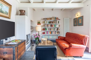 A living room with a television, bookshelves, a red leather sofa, and a vintage cabinet.