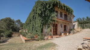 Une maison en pierre dotée d’un balcon, entourée d’une allée en gravier et de verdure.