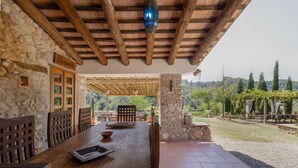 Une table en bois rustique, des chaises, un mur en pierre et une vue sur la campagne.