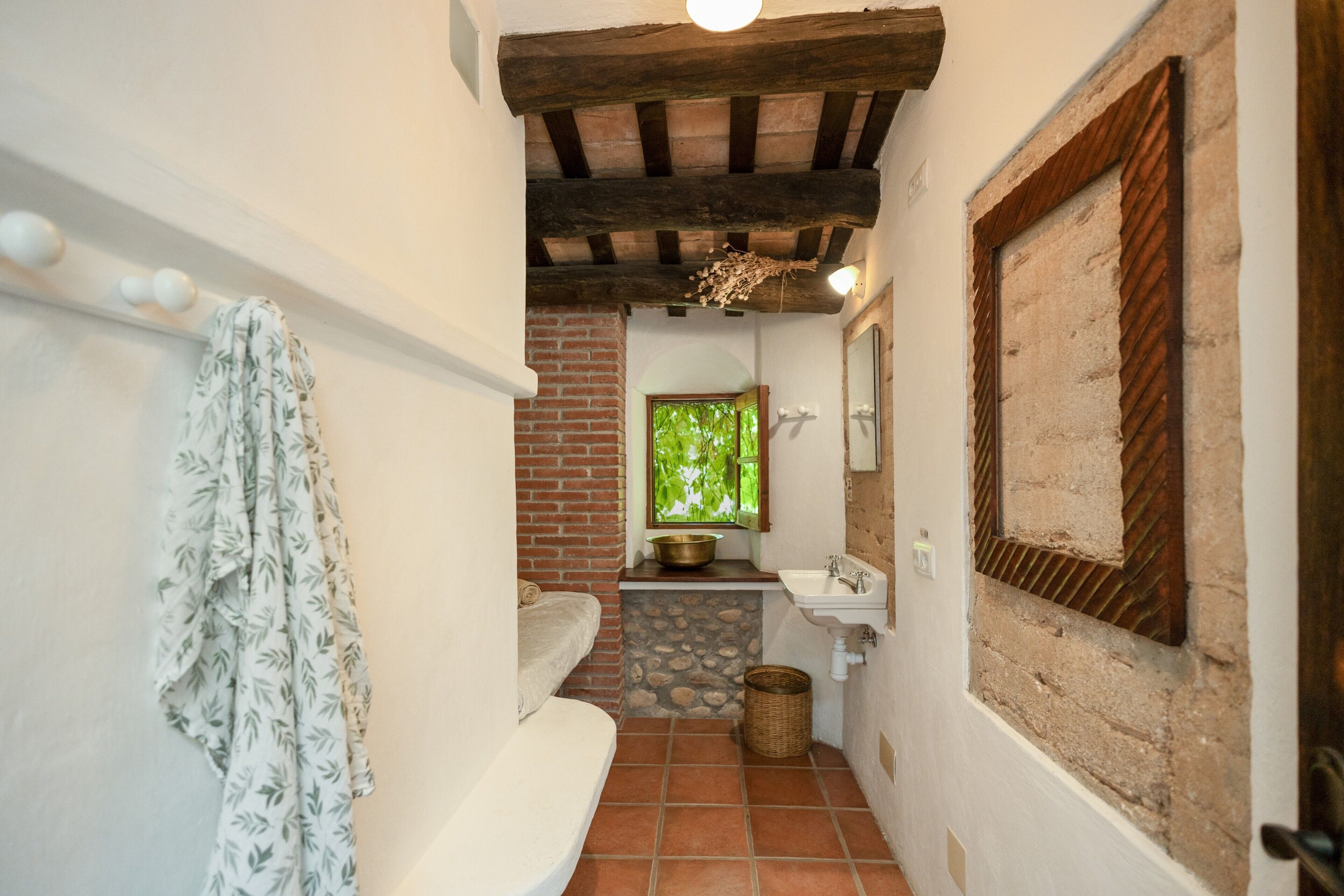 Un baño estrecho con una bañera blanca, un lavamanos y un ventanal con vistas al follaje.