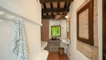 Un baño estrecho con una bañera blanca, un lavamanos y un ventanal con vistas al follaje.