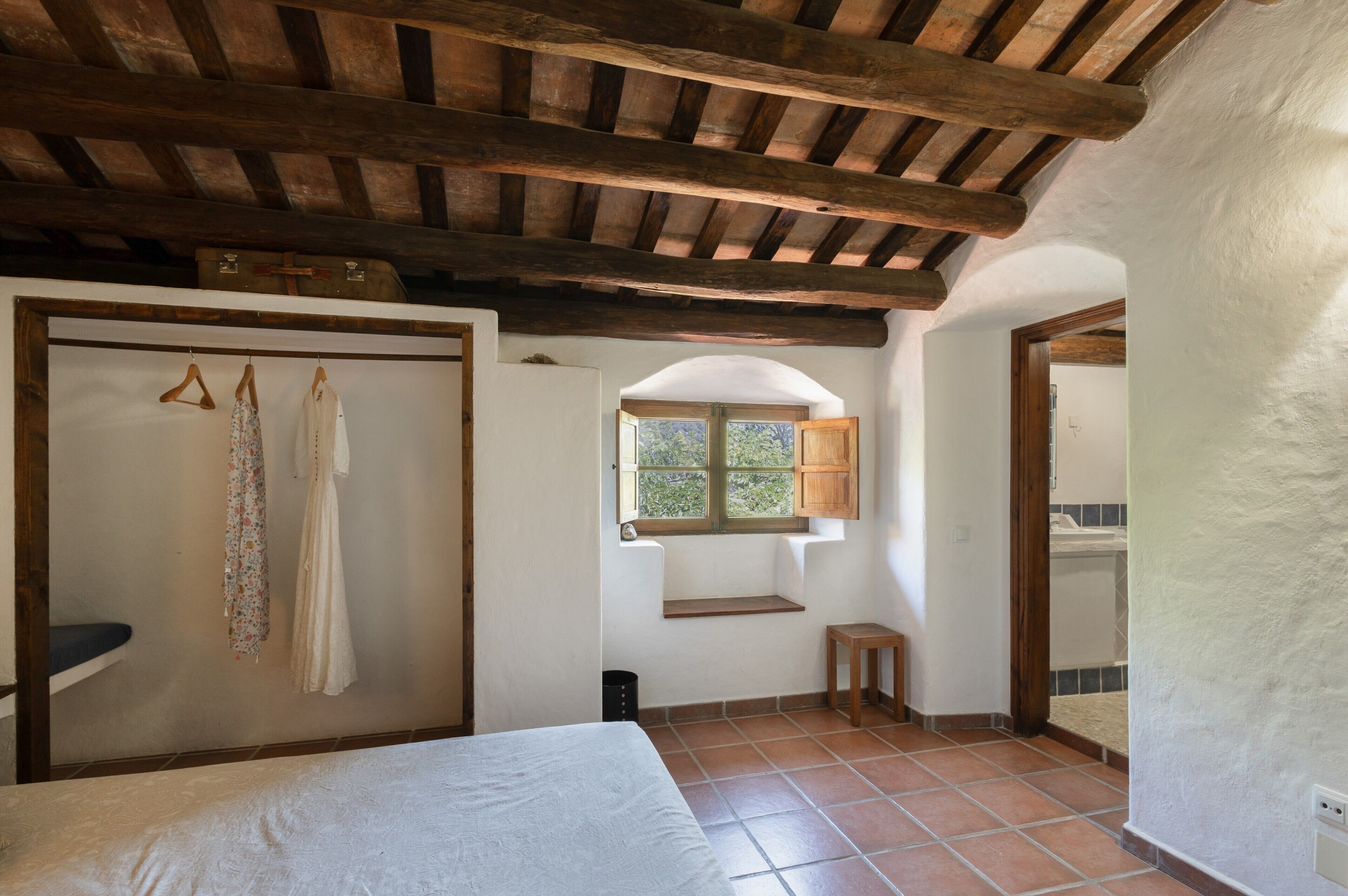 Un dormitorio con cama, techo de madera, ventana y armario.