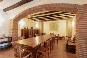 A dining area with a long wooden table, brick arches, and a mural on the wall.