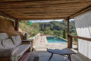 A covered outdoor area with a pool, a wooden bench, and a sofa.