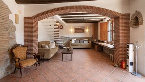 Un intérieur rustique avec une cheminée en briques, un escalier en bois, un canapé et un coin repas.