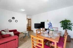 A modern living room with a red sofa, a dining table set for four, a television, and a potted plant.
