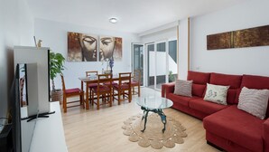 Ett vardagsrum med en röd soffa, ett soffbord i glas, ett matbord med stolar och en tv.