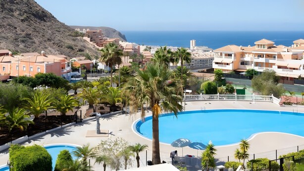 Ett semesterhotell med en stor pool, palmer och byggnader med balkonger med utsikt över havet.