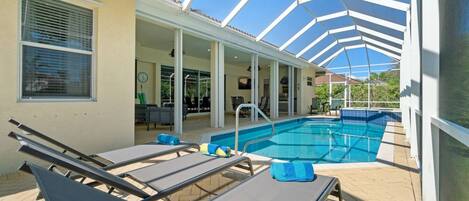 A covered outdoor swimming pool area with lounge chairs and a patio.